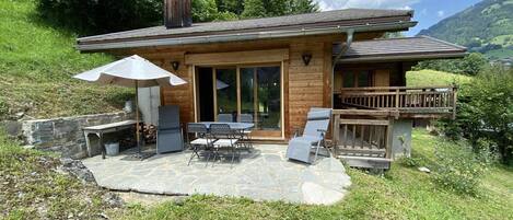 A wooden cabin with a patio, outdoor seating, and a deck overlooking a valley.
