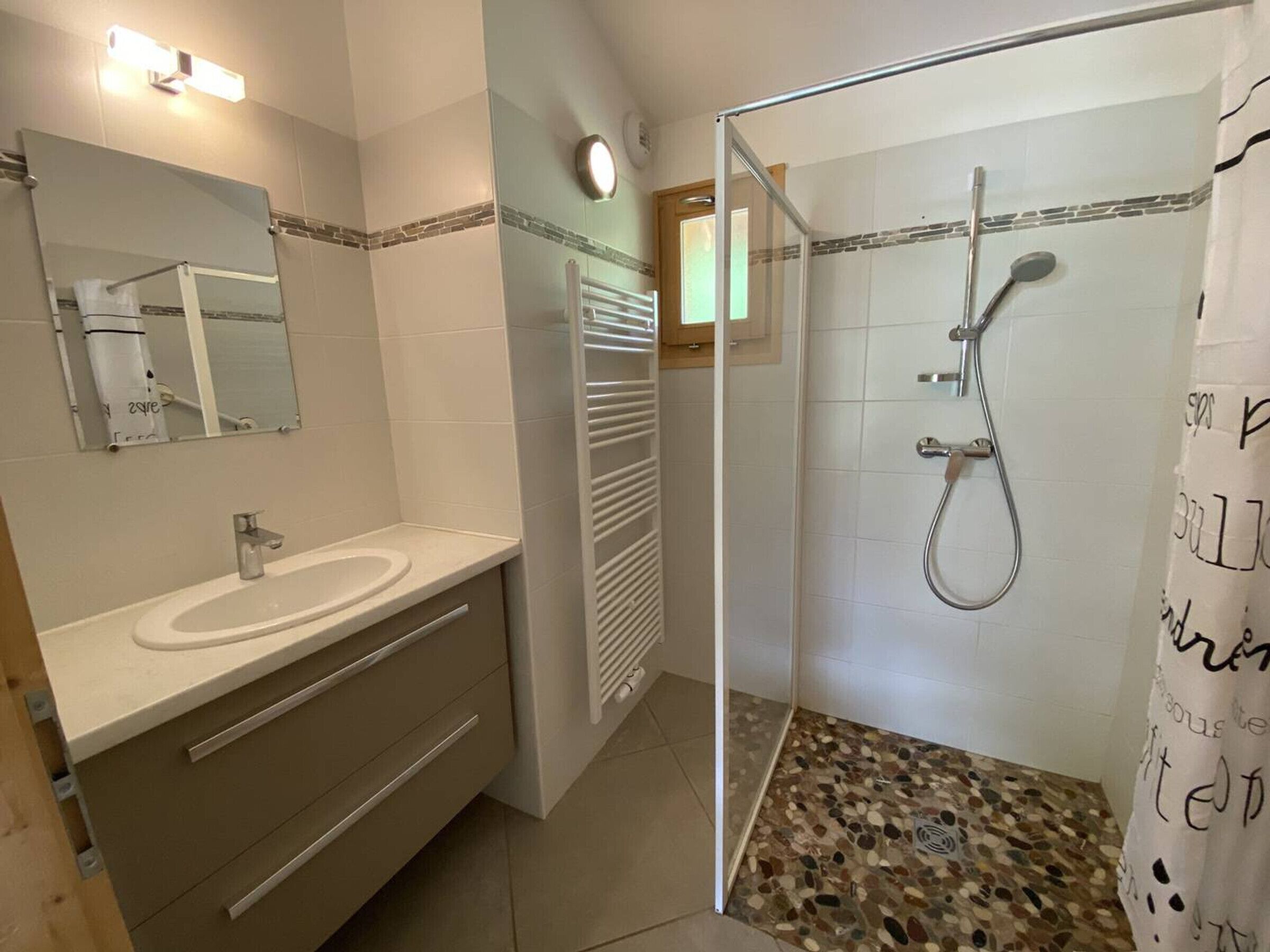 Ein Badezimmer mit Waschbecken, Spiegel, Handtuchhalter, Dusche und einem gemusterten Boden.