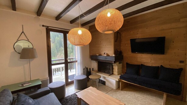 Un salon chaleureux avec une cheminée, un canapé, une table basse et deux lampes suspendues.