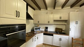 Une cuisine avec des meubles blancs, une cuisinière noire, un four à micro-ondes et une machine à café.
