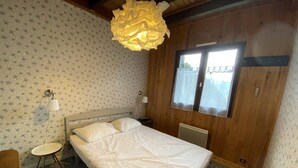 Une chambre à coucher comprenant un lit, une petite table de chevet, une lampe, une fenêtre et un luminaire au plafond.