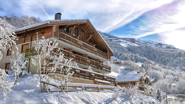 Un chalet en bois doté d’un balcon, entouré d’arbres et de montagnes couverts de neige.