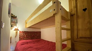 Un lit superposé avec une couvre-lit rouge, une lampe fixée au mur et une tapisserie à motifs.