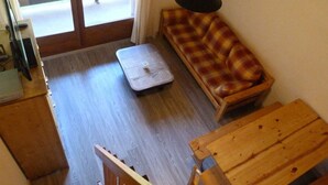 Een kamer met houten vloer, een geruit sofa, een klein tafeltje, een lamp en een schuifdeur naar een buitenruimte.