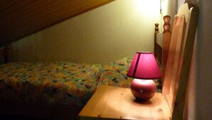 Een kleine, zwak verlichte kamer met een enkel bed, een houten nachtkastje en een lamp.