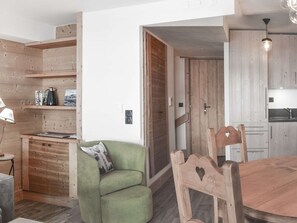 Ein gemütliches Zimmer mit einem grünen Sessel, einem Holztisch und einer Küchenzeile mit Holzschränken und einer Pendelleuchte.