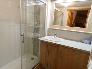 Ein Badezimmer mit einer Duschkabine aus Glas, einem Waschbecken und Holzschränken.