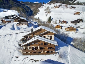 Ein mit Schnee bedecktes Chalet in den Bergen mit mehreren Etagen und Balkonen, eingebettet in eine verschneite Landschaft und umgeben von ähnlichen Gebäuden.