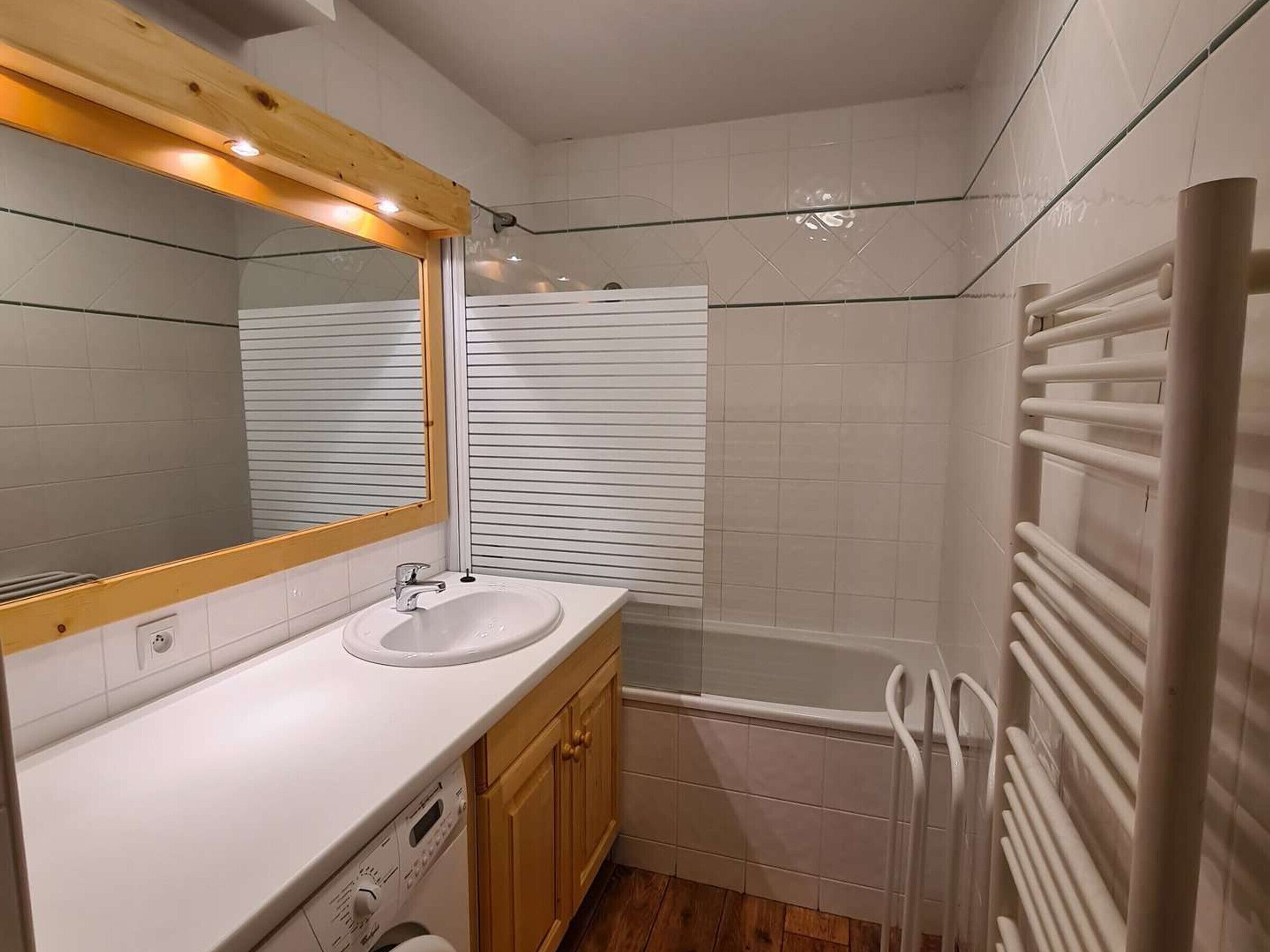 Une salle de bain avec un lavabo blanc, des meubles en bois, un miroir, une baignoire et un porte-serviettes.