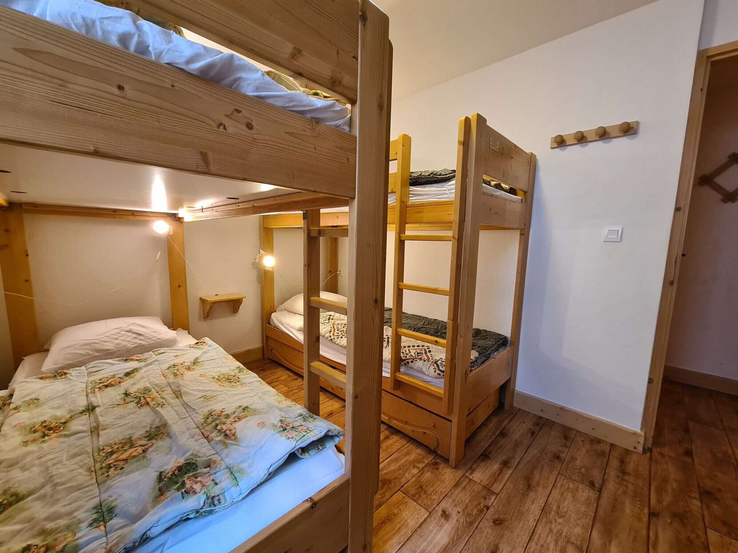 Une chambre avec un lit superposé, un plancher en bois, un lit simple avec une couette à motifs floraux et une petite étagère.