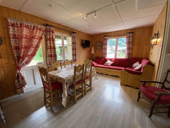 Ein Holzinnenraum mit einem Esstisch, Stühlen, einem roten Sofa und einem Fernseher.