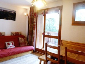 Ein gemütliches Zimmer mit einem roten Sofa, Holzsesseln, einem Fenster mit Vorhängen und einem Bild an der Wand.