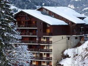 Ein mehrstöckiges Holzgebäude mit Balkonen, umgeben von schneebedeckten Bäumen und Bergen.