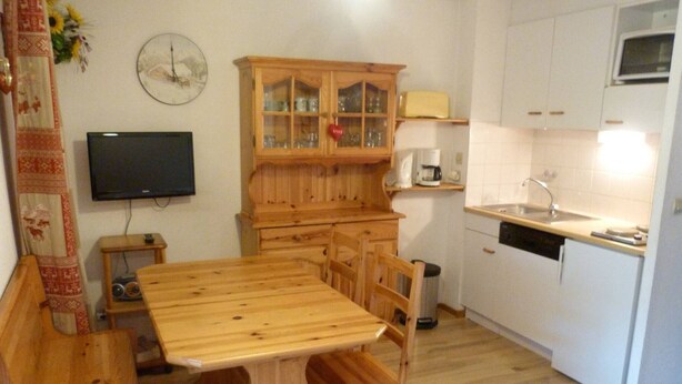 Ett kök med ett träbord, stolar, ett skåp med glasdörrar, en mikrovågsugn och en klocka på väggen.