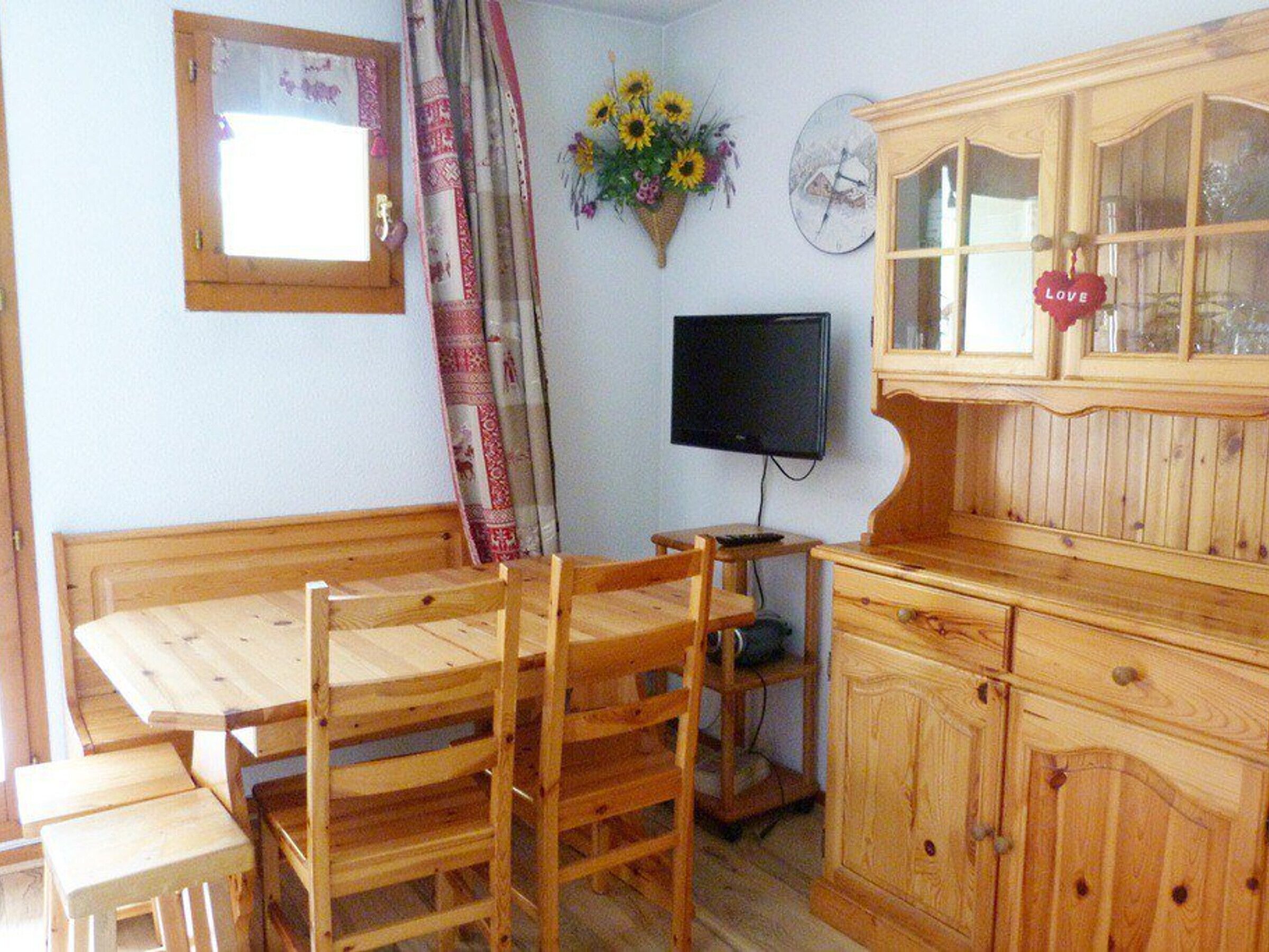 Una habitación con una mesa de comedor de madera, sillas, un televisor, un armario y un reloj de pared.