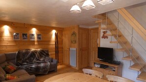 A wooden cabin interior with a sofa, a dining table, a television, and a staircase. - Apartment at the foot of the slopes - 6 guests (Arêches-Beaufort)
