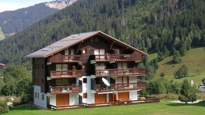 A multi-story wooden chalet with balconies, set in a mountainous area with dense forest. - Apartment at the foot of the slopes - 6 guests (Arêches-Beaufort)