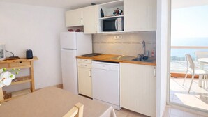 A compact kitchen with a microwave, refrigerator, and dishwasher, a wooden table with chairs, and a view of the sea through a balcony. - Studio cab, AC, sea view, parking - 4 guests (Sète)