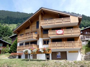 Un immeuble en bois à plusieurs étages, doté de balcons, d’une jardinière et d’une enseigne indiquant la présence d’un restaurant.
