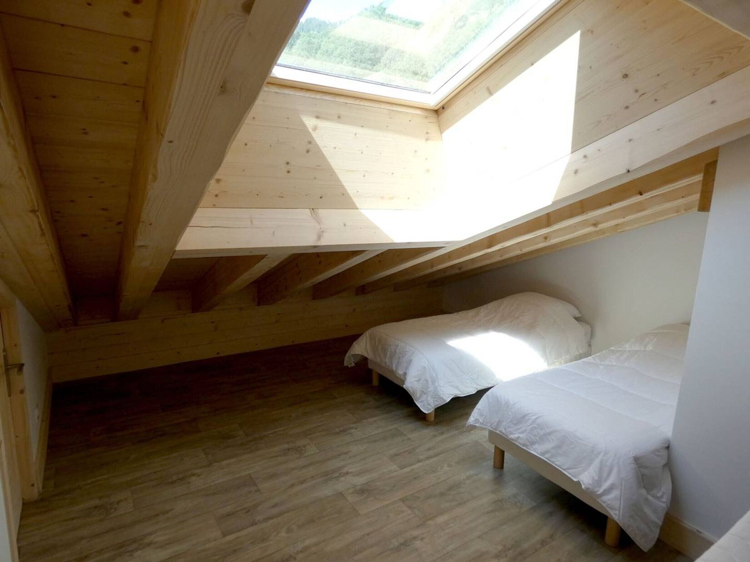 Un pequeño dormitorio en el ático con dos camas, vigas de madera y un tragaluz.