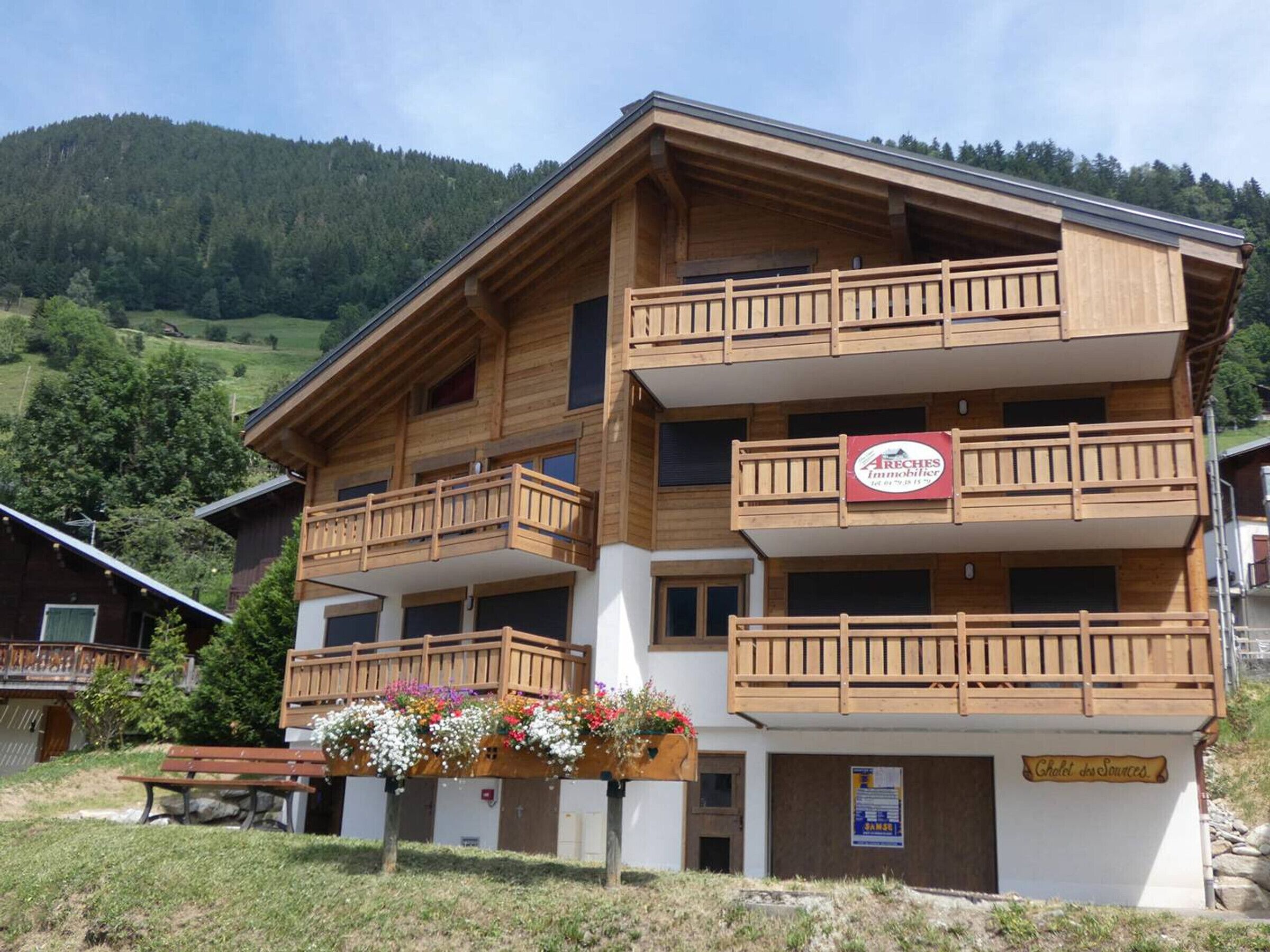 Un immeuble en bois à plusieurs étages, doté de balcons, avec une enseigne indiquant « AReches Immobilier » et une autre indiquant « Gîte des Sources ».