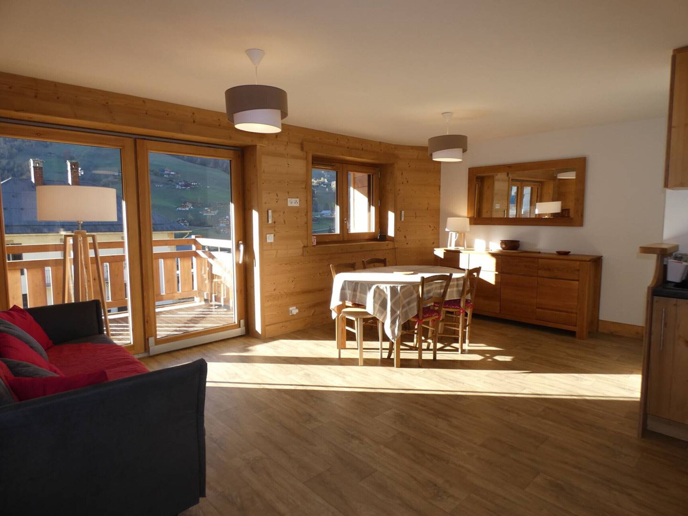 A cozy cabin interior with a dining area, wooden walls, and a large sliding glass door leading to a balcony.