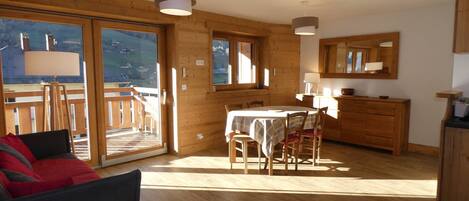 A cozy cabin interior with a dining area, wooden walls, and a large sliding glass door leading to a balcony.