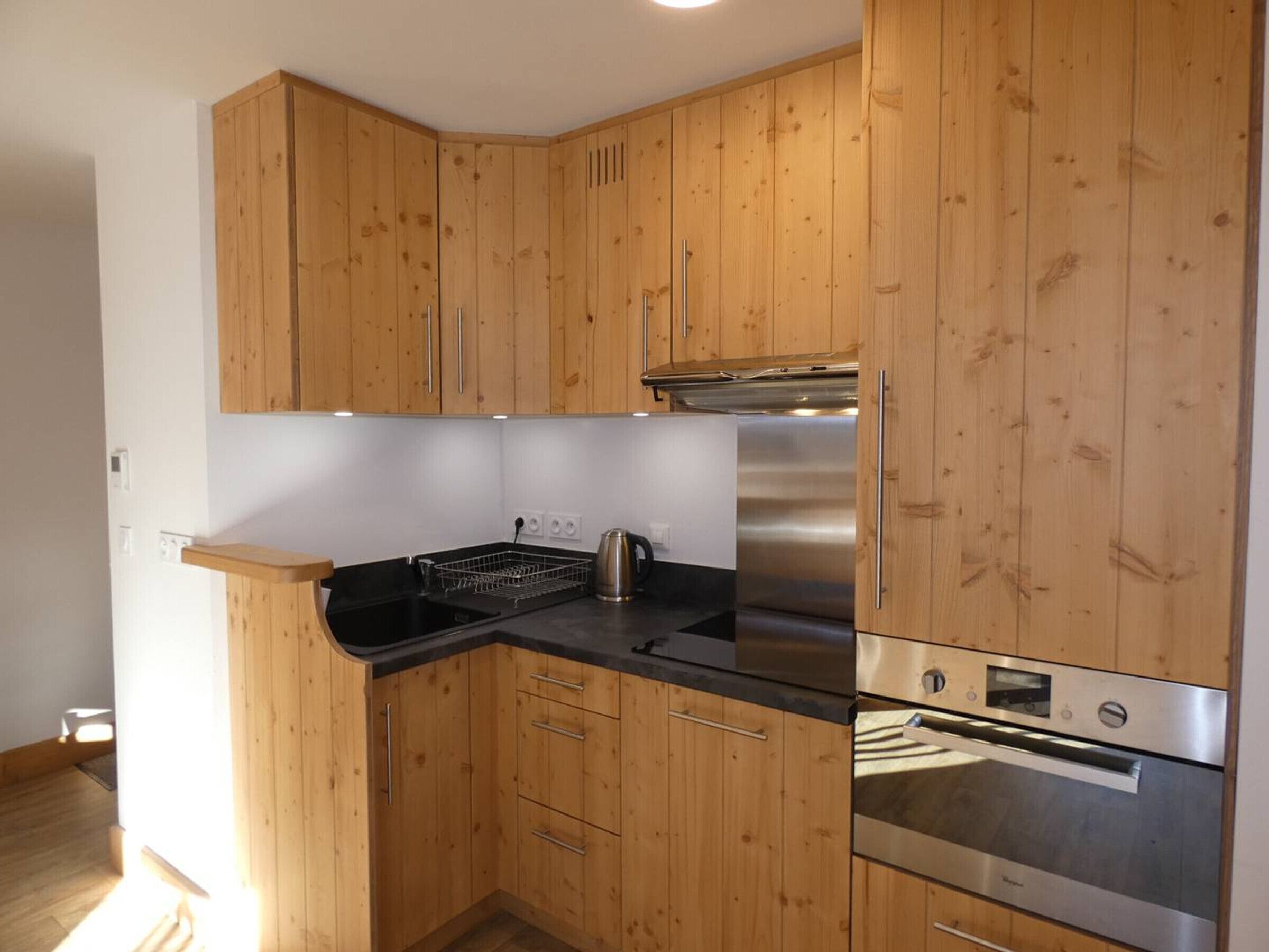 A compact kitchen with wooden cabinets, a stainless steel refrigerator, and an oven.