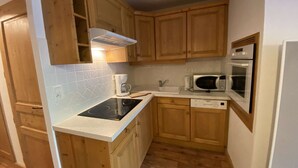 A compact kitchen with wooden cabinets, a microwave, an oven, a coffee maker, and a dishwasher. - Cozy apartment near shuttles - 4 guests (Arêches-Beaufort)