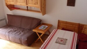 Ein Schlafzimmer mit einem Holzbett, einem kleinen Nachttisch, einem braunen Sofa und einem Holzschrank darüber.