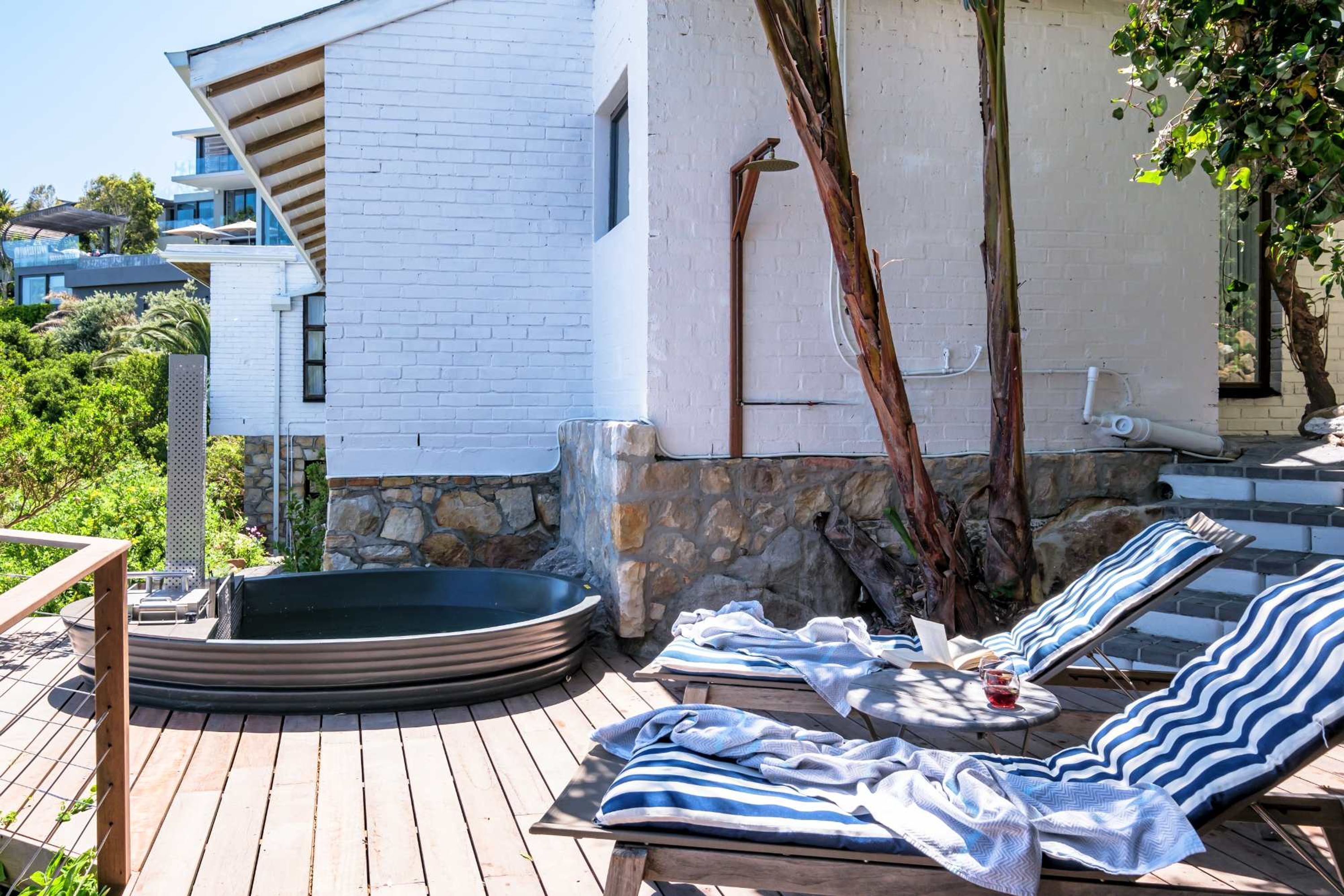 A wooden deck with lounge chairs and a hot tub, a white building with stone accents, and a tree.