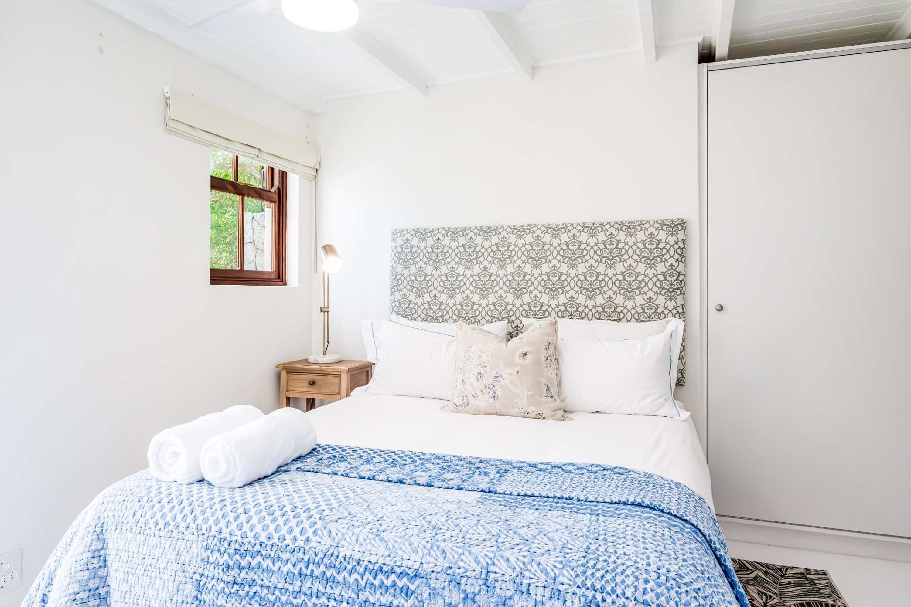 A bedroom with a bed, a nightstand, a window, and a wardrobe.