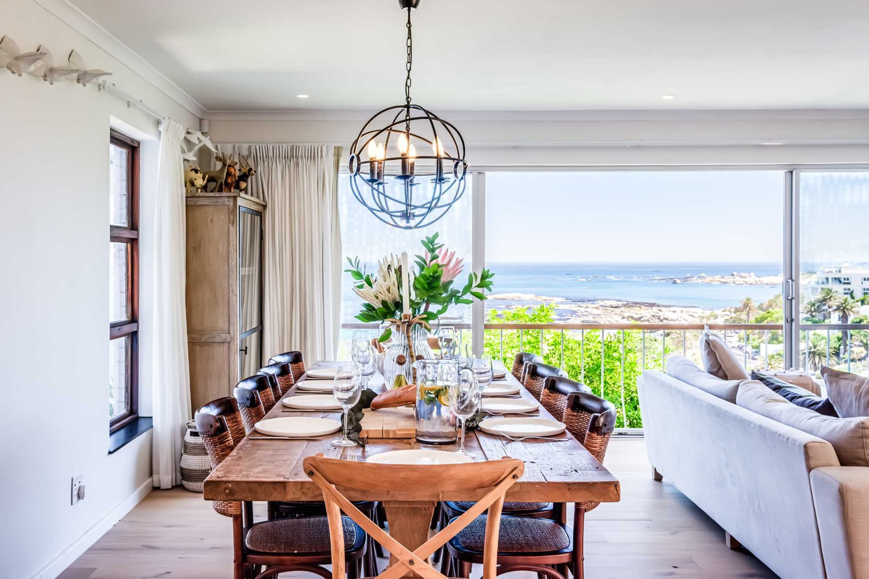 A dining area with a table set for six, a chandelier, and a view of the ocean.