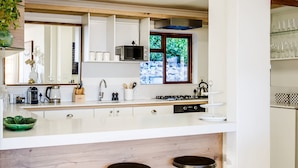 Una cocina moderna con armarios blancos, un microondas, un hervidor y un lavamanos. Hay tres taburetes debajo de la encimera.
