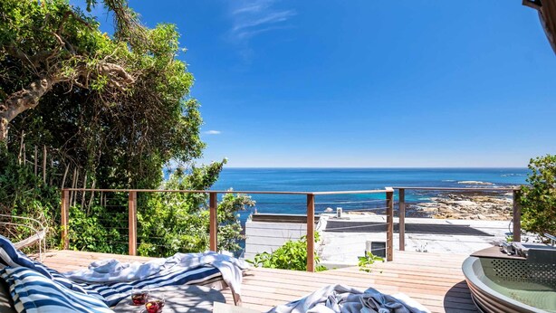 Terraza de madera con vistas al mar, jacuzzi y sillas de descanso.