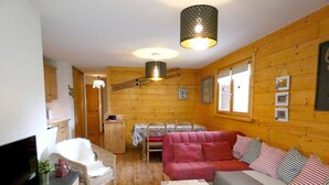 Ett mysigt rum inrett som en stuga, med en soffa, en tv, ett matbord och ett träpanelat tak.