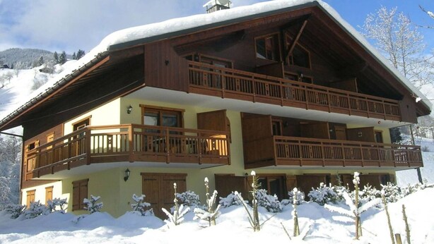 En tvåvånings chalet med träbalkonger, ett sluttande tak och en snötäckt omgivning.