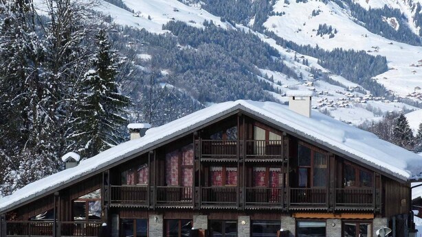 Ein Chalet mit steilem Dach, Holzbalkonen und Blick auf die Berge.
