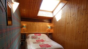 Ein gemütliches Zimmer mit schrägen Wänden, Holzwänden, einem Bett mit einer Bettdecke, zwei Nachttischlampen und einem Dachfenster.