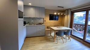 Een moderne keuken met grijze kastjes, een houten eettafel met stoelen, en een televisie aan de muur.