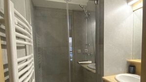 Een badkamer met een douche in een glazen cabine, een witte wastafel en een houten kast.