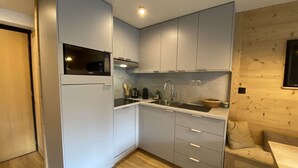 Een kleine keuken met een magnetron, fornuis, spoelbak en houten wandbekleding.