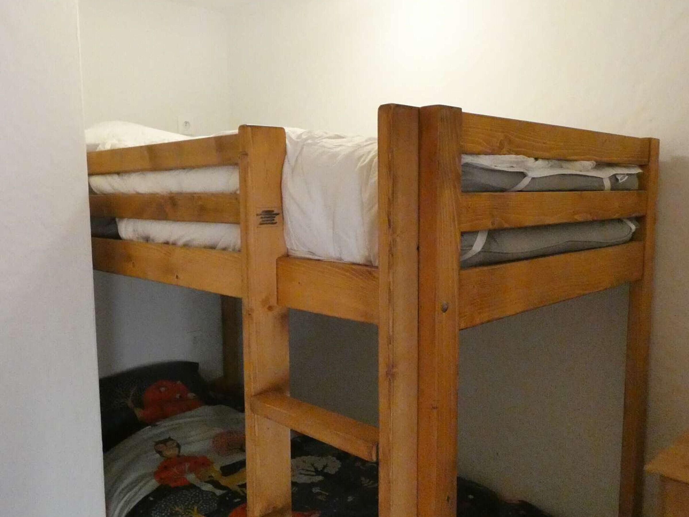 A bunk bed with white bedding, a wooden frame, and a lower bunk with a patterned blanket.