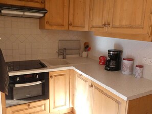 A kitchen with wooden cabinets, a stove, a sink, and a coffee maker. - Cozy apartment - 4 guests (Arêches-Beaufort)