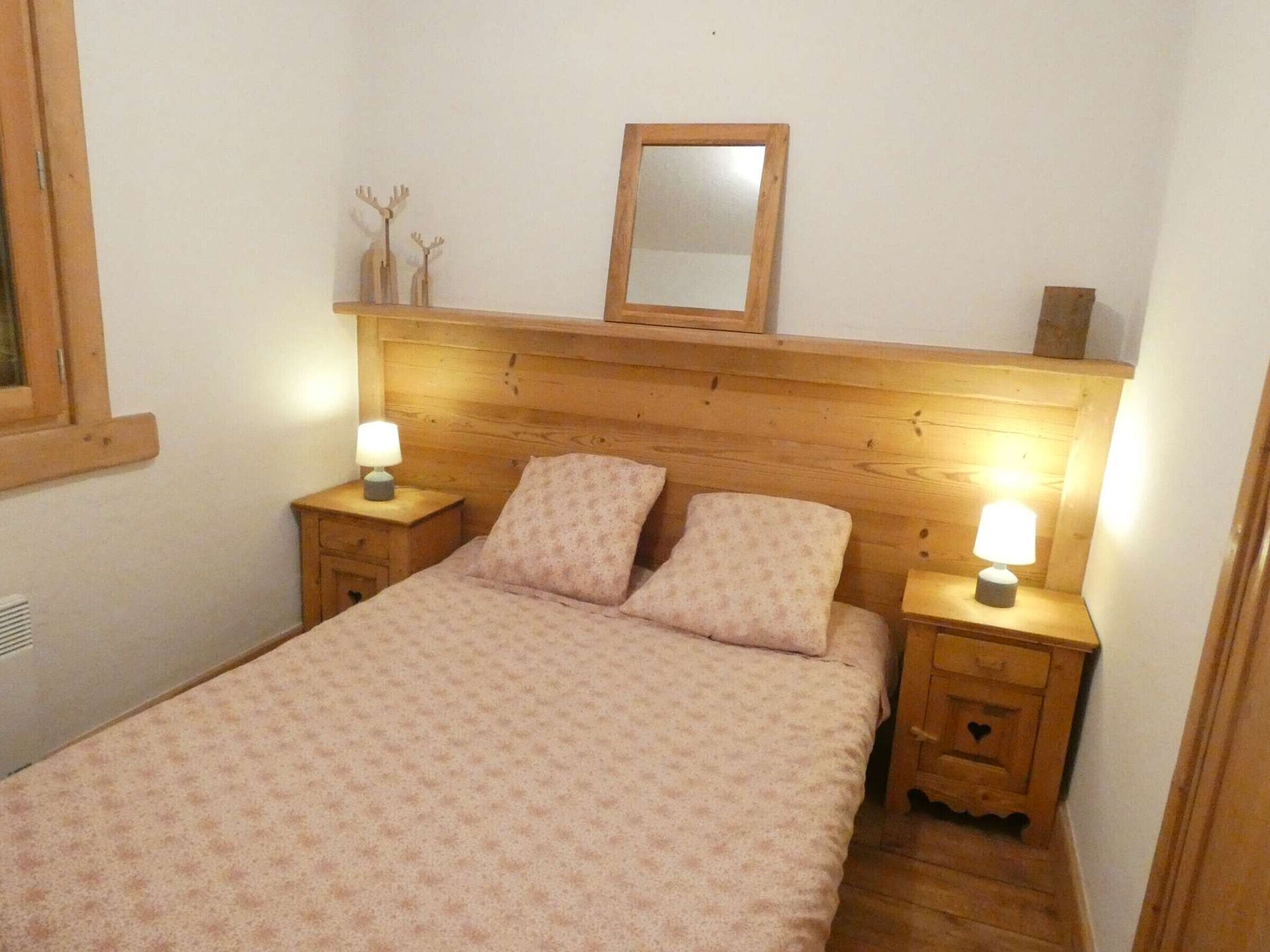 Een slaapkamer met een houten hoofdbord, twee nachtkastjes met lampen, een bed met beddengoed met een patroon, een spiegel en decoraties aan de muur.