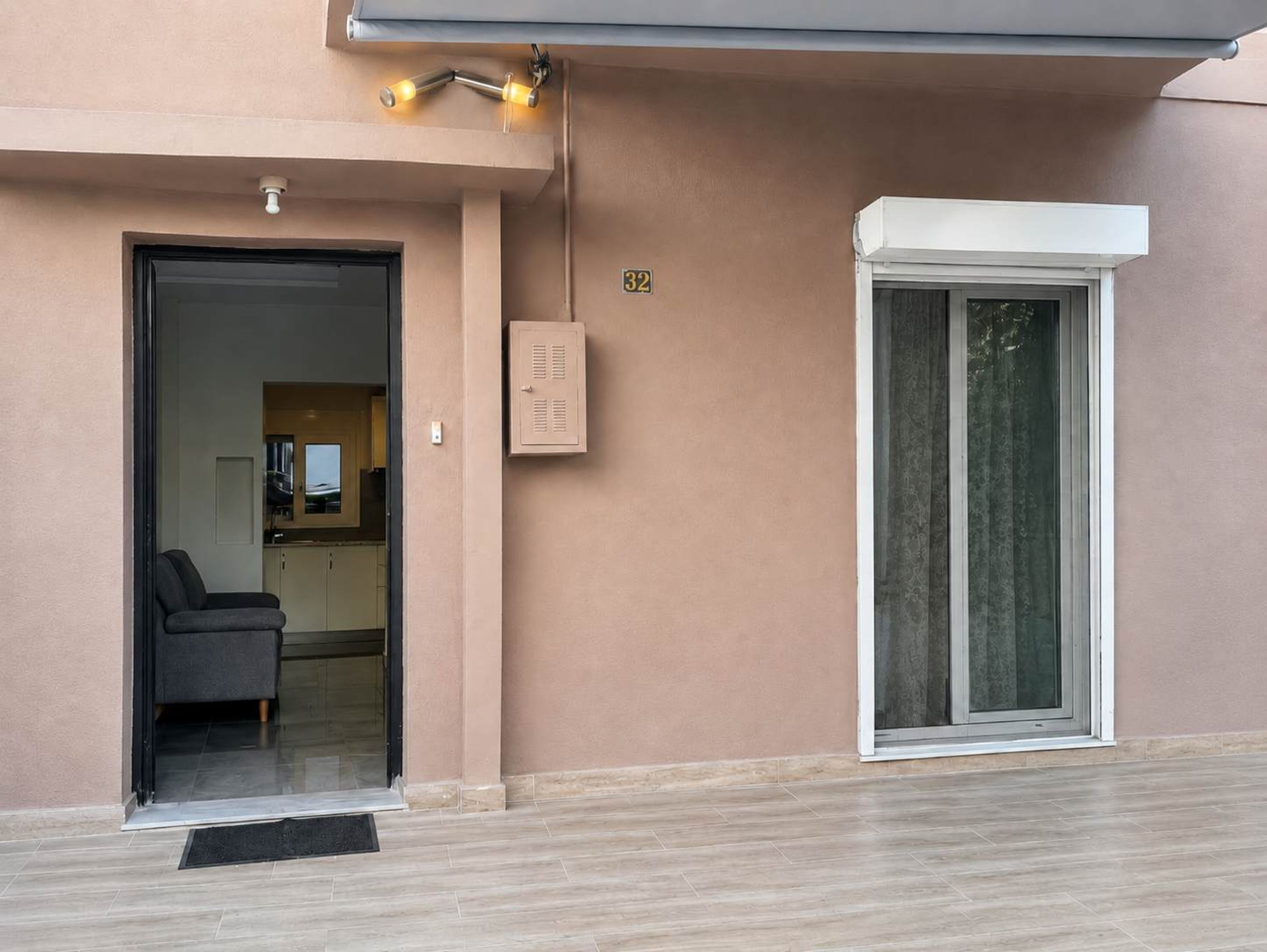 Une entrée d’immeuble avec une porte, un petit espace d’attente, un coffret électrique et une fenêtre.