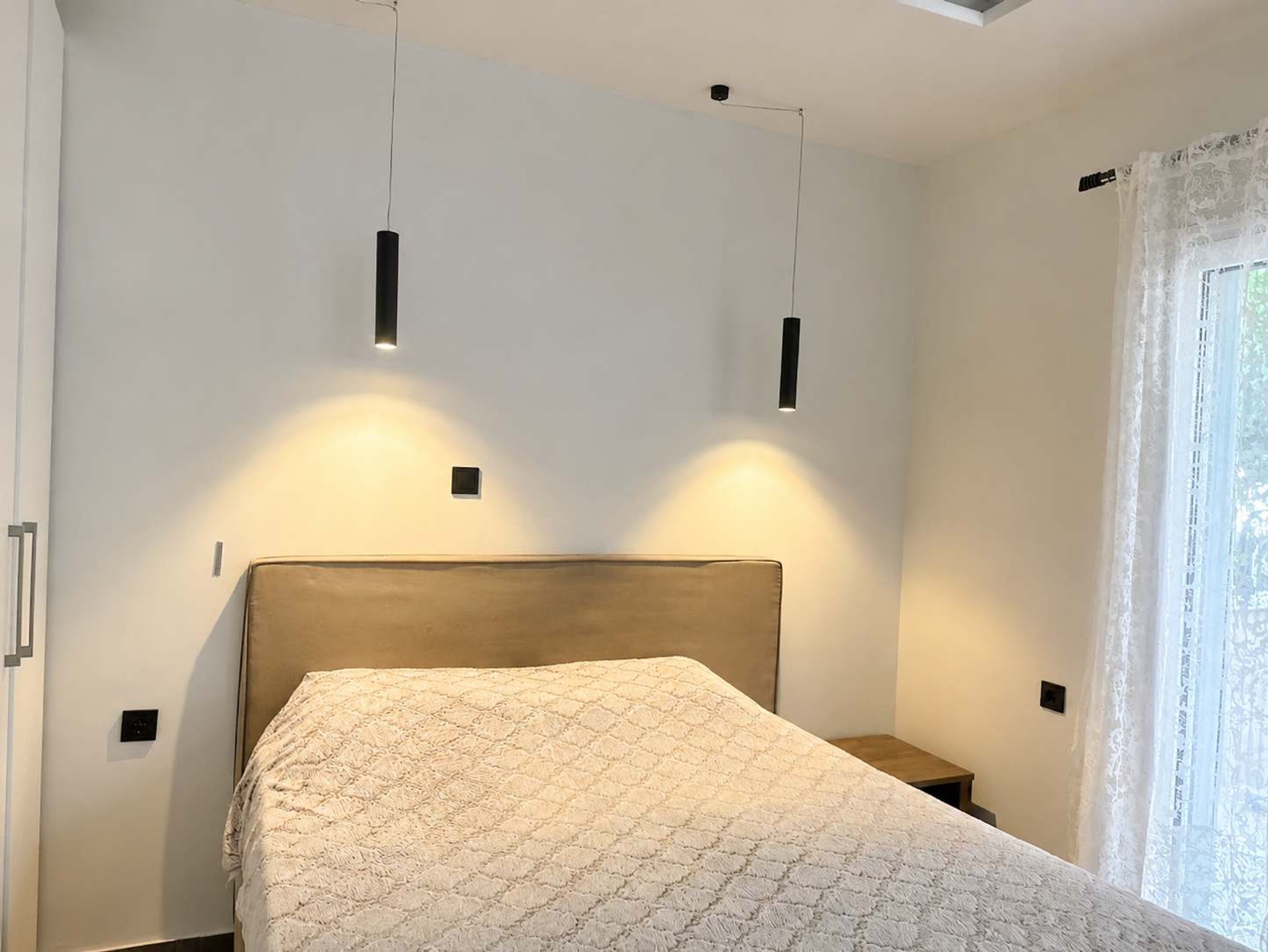 A bedroom with a bed, bedside tables, and pendant lights.