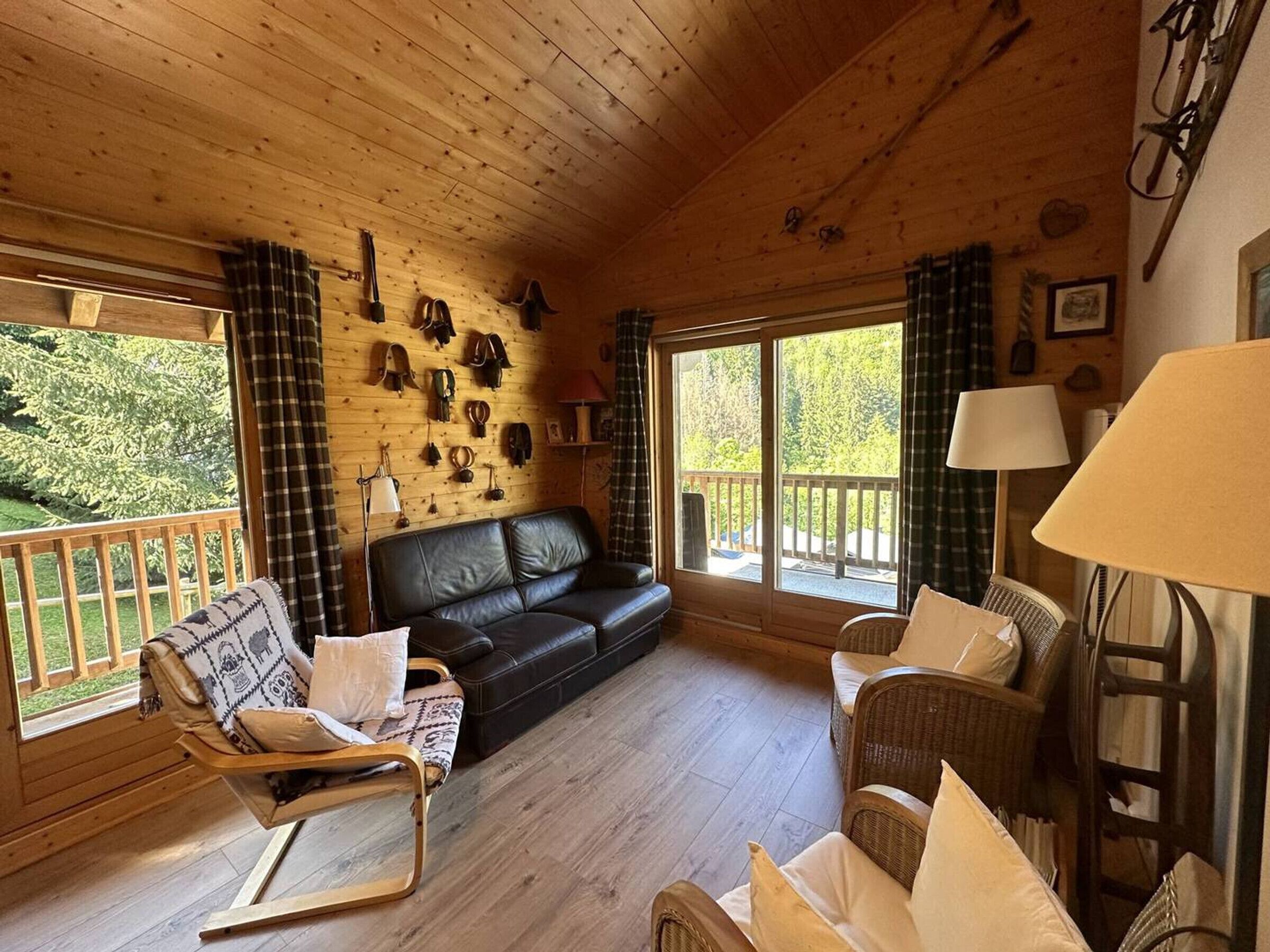 Ein Interieur einer Holzhütte mit einer schwarzen Ledersofa, zwei Korbstühlen, einem Holzboden und einem an der Wand befestigten Schuhregal.