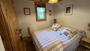 Een slaapkamer met een houten plafond, een bed met beddengoed met een patroon, een raam met uitzicht en een lijst met een afbeelding aan de muur.