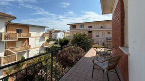 Ein Balkon mit Tisch und Stühlen, Blick auf benachbarte Gebäude und ein umzäunter Gartenbereich.